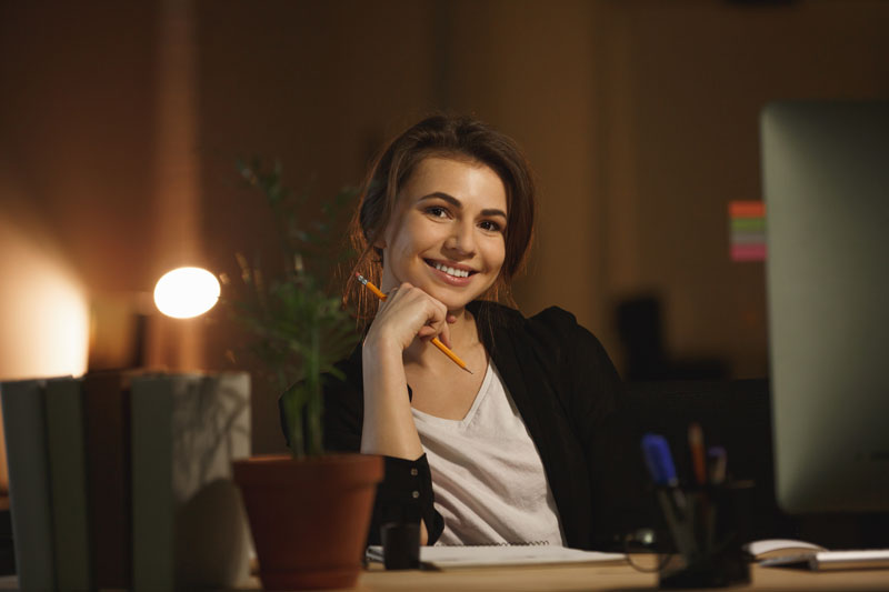 Mulher empresária de terno preto sorridente e feliz sentada em frente ao seu computador