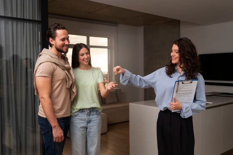 Corretora passando a chave as mão de uma mulher que está com seu marido em uma sala de uma casa vazia.